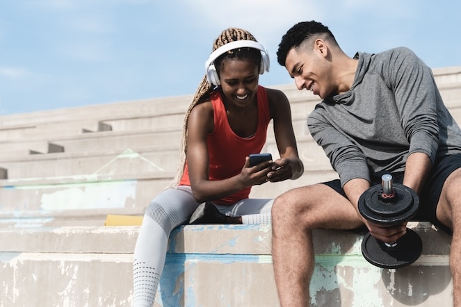 Two athletes sitting in stands after a workout using social media to promote something good.