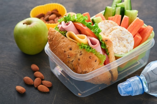 Healthy lunch sandwich with turkey lettuce and tomato, crackers, veggies, an apple, nuts and some water.