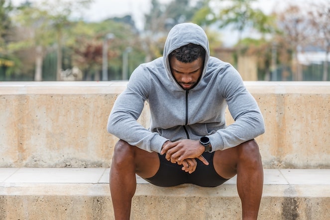 Depressed African American athlete wearing a gray hood and sitting on the steps