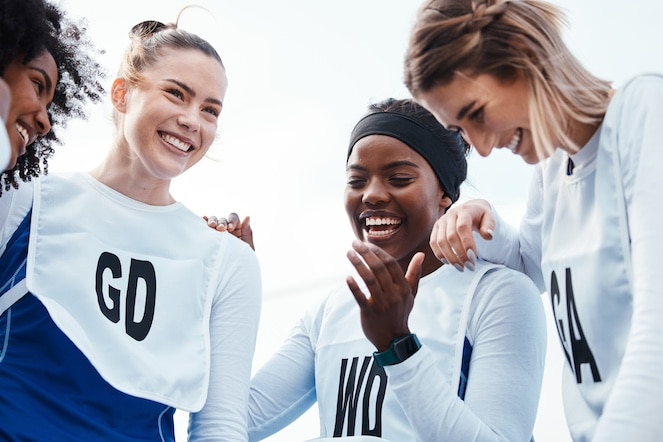 Diverse Netball team laughing and together in a team huddle.