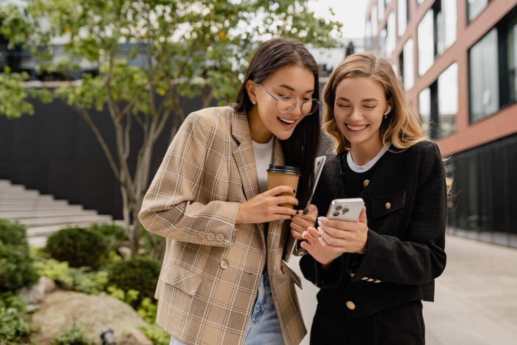 Two young girls looking at a cell phone and happy about something they see. 