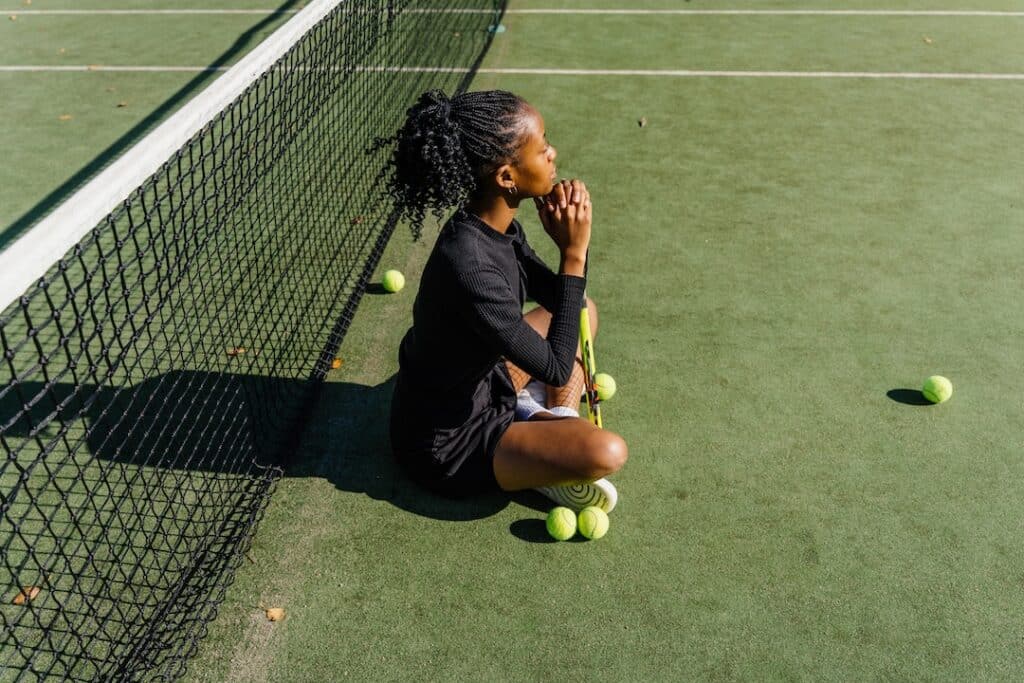 Tennis athlete sitting on a court leaning on her tennis racket reflecting on the match.
