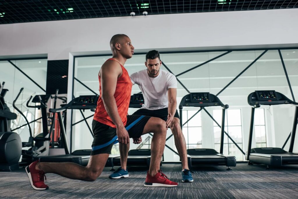 Male athlete in a perfect lunge position with a coach overseeing him.