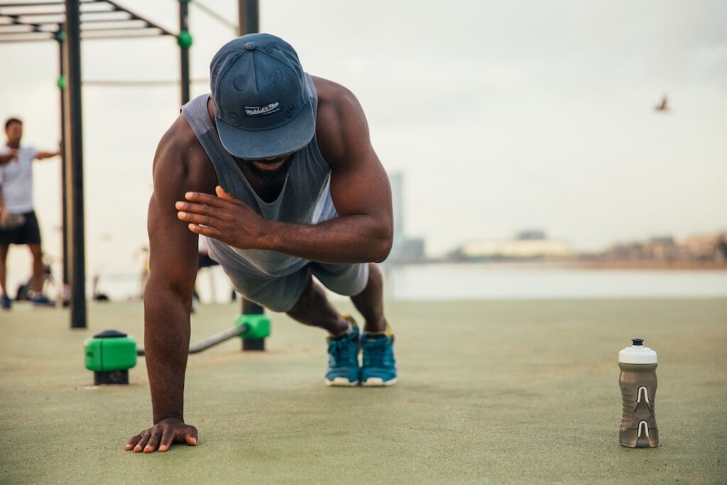 Athlete working out on the grass outside and doing a one armed pushup.
