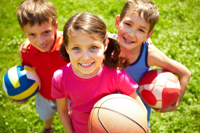 Three young children holding three different balls and smiling at the camera.