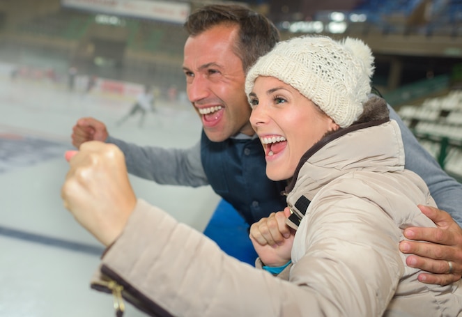 Two parents in the stands at an ice hockey game cheering for their athlete.
