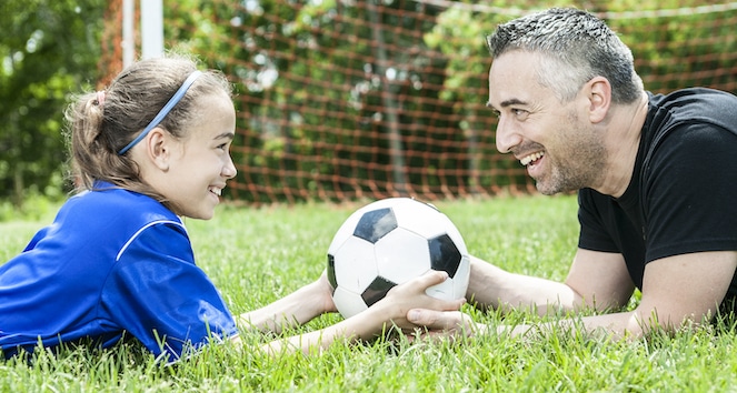 Dad and daughter smiling and holding soccer ball together.