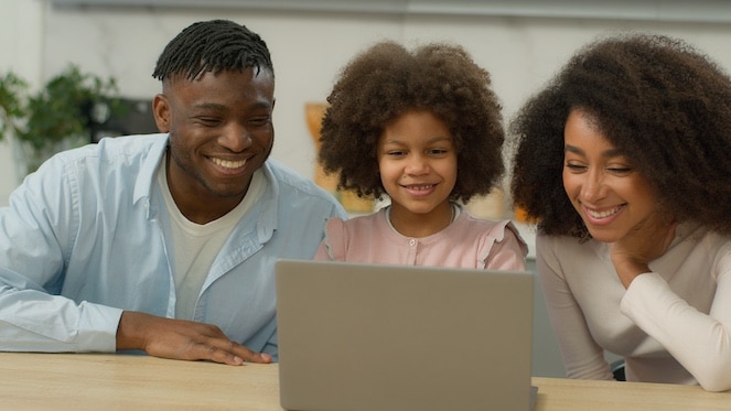 Parents with their young daughter looking at a computer and smiling.