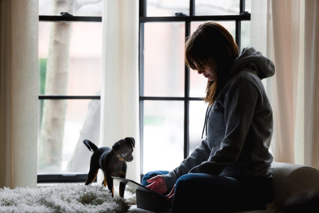 Teenager sitting on her bed with her dog and working on her Ipad.